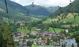 A picturesque mountain landscape with hills and green meadows. In the background, small houses and the clear mountains are visible.