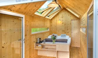 A cozy room with wood paneling. It includes a bed, a table, and large windows for plenty of daylight.