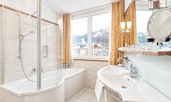A modern bathroom with a shower cubicle and a bathtub. Large windows offer a beautiful view of the mountains.