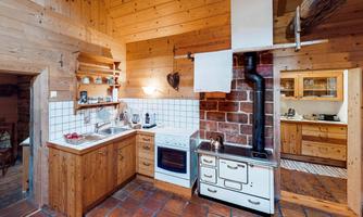 A cozy wooden kitchen with a traditional design. There is a stone oven, a modern cooking station, and plenty of storage space.