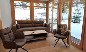 A modern living room with a cozy couch and two armchairs. Large windows provide a view of a snowy landscape.