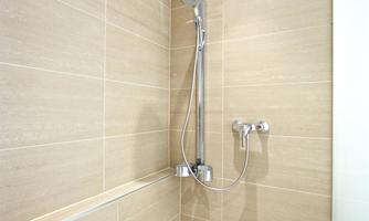 A modern shower cabin with bright tiles and a clear showerhead. The walls are designed to be simple and elegant.