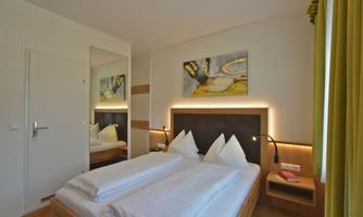 A modern bedroom with two beds and a light wall color. The room has a large mirror and appealing artworks on the wall.