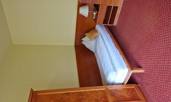 A simple bedroom with a single bed and a nightstand. A wardrobe and a dresser complete the furnishings.