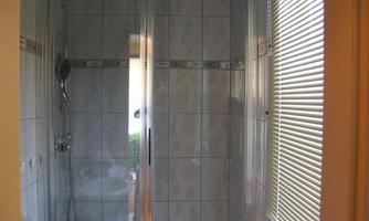 A modern bathroom with a glass shower cabin and tiled walls. Daylight enters through a window with blinds.