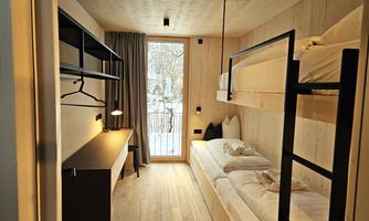 A modern room with wooden paneling and two beds. Large windows bring in plenty of daylight.