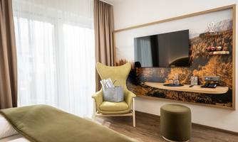 A modern hotel room with a comfortable chair and a large television on the wall. Soft colors and a pleasant atmosphere create an inviting space.