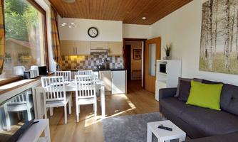 A bright and modern open-plan kitchen with a cozy living room. The decor is simple and inviting, featuring a dining area and a comfortable couch.