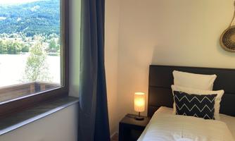 A cozy bedroom with a single bed and a modern bedside lamp. The window offers a beautiful view of the landscape.