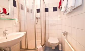 A small bathroom with a shower, a sink, and a toilet. The walls are lightly tiled and there are towels on the wall.