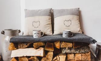 A cozy seating area with two cushions on a wood stack. On top are two cups and a gray blanket.