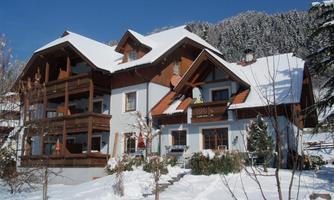 A charming wooden house in the snow with a red roof. Surrounded by snow-covered trees and mountains.
