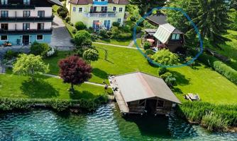 A beautiful garden by the water with a small building and green lawn. In the background, several villas and trees can be seen.