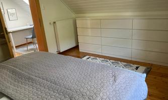 A cozy bedroom with a bed and a bright dresser. In the background, a desk with a chair can be seen.