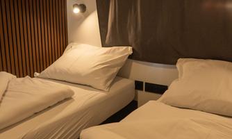 A cozy bedroom with two beds and modern wooden paneling. The bedding is fresh and white, and a gentle lamp provides pleasant light.