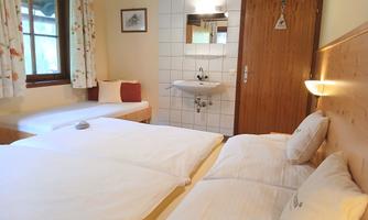 A cozy room with two beds and a small sink. There is a window view and friendly, bright colors.