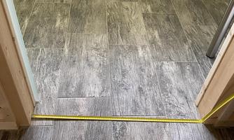 A room with a gray tiled floor. A measuring tape lies on the floor between two entrances.