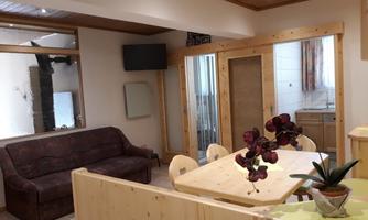 A cozy living space with a couch, a dining table, and an open kitchen. The room has bright walls and wood paneling, creating a warm atmosphere.