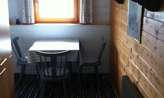 A bright room with a table and chairs as well as a window that lets in daylight. The floor is made of wood, and various pieces of furniture are visible.