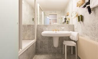 A modern bathroom with gray tiles and a shower. There is a sink, towels, and a radiator.