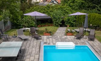A beautiful outdoor area with a blue pool and sunny loungers. Shady umbrellas and green plants complete the relaxing atmosphere.