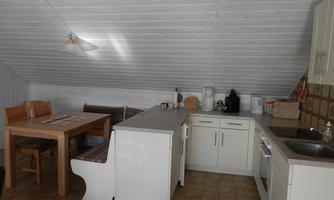 A cozy kitchenette in an attic with a dining area. The walls are painted in light colors and there are basic kitchen appliances.