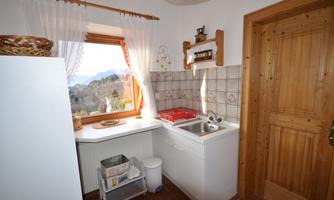 A cozy kitchen with a window that offers a view of the mountains. The walls are tiled and there are wooden shelves as well as a sink.