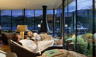 A cozy living room with large windows that offers a beautiful view of the landscape. A couple relaxes on a sofa and enjoys the atmosphere.