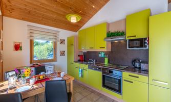 Modern kitchen with yellow cabinets and wooden ceiling. A dining table is set with flowers and dishes.