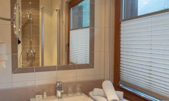 A modern bathroom with a sink, towels, and large windows. The shower is visible in the background.