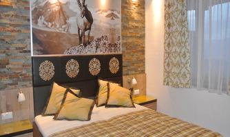 A cozy bedroom with a large bed and decorative pillows. On the wall hangs a picture of a ibex, surrounded by rustic stone.