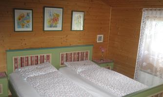 A cozy bedroom with two beds and a wooden wall. Pictures hang on the wall, and there is a small lamp on the nightstand.