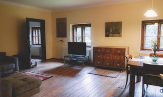 A cozy living room with wooden floor and warm colors. There is a television, a dresser, and a dining table with chairs.