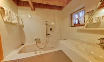 A modern bathroom with a bathtub and a sink. The walls are tiled in white, and there are wooden details on the ceiling.