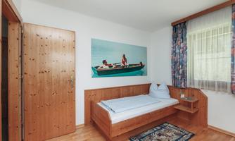 A simple bedroom with wooden furniture and a single bed. On the wall hangs a picture of two people in a boat on water.