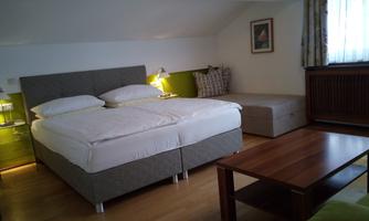 A cozy bedroom with a large double bed and a seating area. The walls are light, and a wooden table complements the decor.