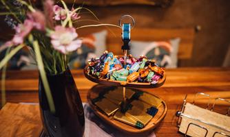 A wooden stand with colorful candies is on a table. Next to it, there is a vase with fresh flowers.
