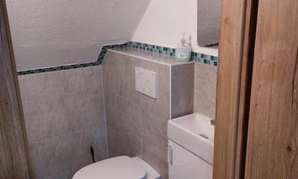 A modern bathroom with a toilet and a small sink. The walls are tiled and there is a mirror.