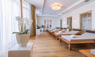 A modern wellness area with several loungers and plants. Large windows let in plenty of light and create a relaxed atmosphere.