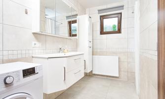 A modern bathroom with a sink and washing machine. Bright tiles and a window provide natural lighting.