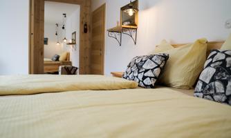 A cozy bedroom with two beds and yellow bed linen. In the background, a modern decor with a mirror and warm lighting is visible.