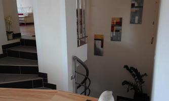 A cozy entrance area with a modern staircase and decorative pictures on the wall. A plant is visible in the background.
