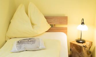 A cozy bedroom with a bed, yellow pillows, and a bedside lamp. The walls are painted in a warm shade of yellow.