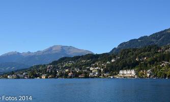 A picturesque lake with green-covered shores and calm water. In the background, majestic mountains rise under a clear blue sky.
