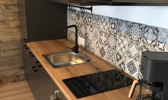 A modern kitchen with a wood countertop and a stylish tiled backsplash. The equipment includes a stove, a sink, and a coffee machine.