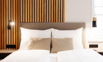 A modern bedroom with a cozy bed and decorative pillows. The woodcuts on the wall give the room a warm atmosphere.