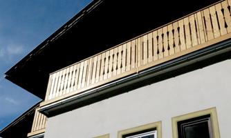 A modern house with a wooden balcony and sleek lines. The sky is blue with few clouds.
