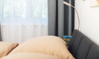 A cozy bedroom with two large pillows and a modern bed. Next to the bed is a reading lamp and a book is visible.