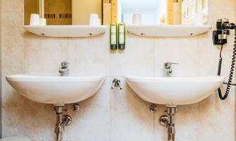 A modern bathroom with two sinks and bright tiles. On the wall, there are care products and a telephone.