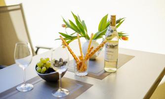 An elegant table with two wine glasses, a bottle of white wine, and snacks. A bowl of grapes and fresh tulips complete the arrangement.